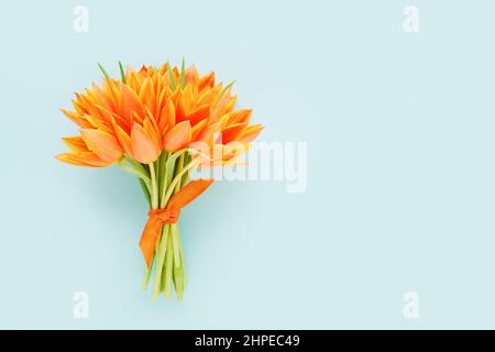 Bouquet de tulipes orange décoré de ruban sur fond bleu clair. Carte de vœux Banque D'Images