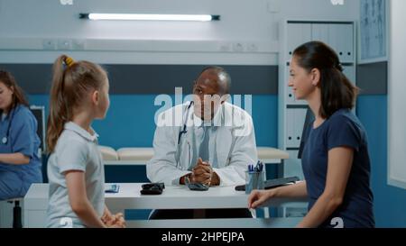 Généraliste saluant la mère et l'enfant au cabinet, assistant à un rendez-vous de contrôle. Pédiatre ayant discuté avec une petite fille et un parent lors d'une visite d'examen médical. Banque D'Images