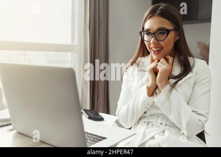 Belle jeune femme d'affaires heureuse, femme utilisant un ordinateur portable et souriant en travaillant à l'intérieur. Bureau à domicile pendant la quarantaine du coronavirus ou du Covid-19. Comm Banque D'Images