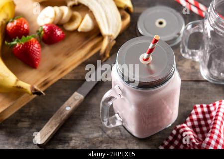 Smoothie frais à la fraise et à la banane dans un pot sur une table en bois Banque D'Images