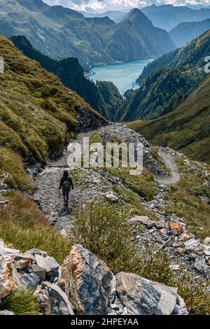 Paysage alpin avec un chemin serpentant à travers les montagnes et un lac au loin. Une fille marche sur le chemin, avec elle de retour au photographe et se dirige vers le lac. Photo de haute qualité Banque D'Images