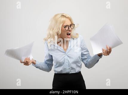 Jeune femme d'affaires stressée avec des papiers se sentant en colère ou souffrant d'une panne nerveuse, debout sur fond clair Banque D'Images