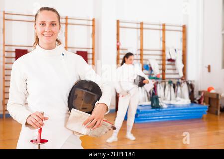 Jeune femme souriante en uniforme debout dans la salle d'escrime Banque D'Images