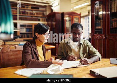 Portrait d'une femme mature professeur tutorat afro-américain étudiant en intérieur de bibliothèque classique à l'université Banque D'Images