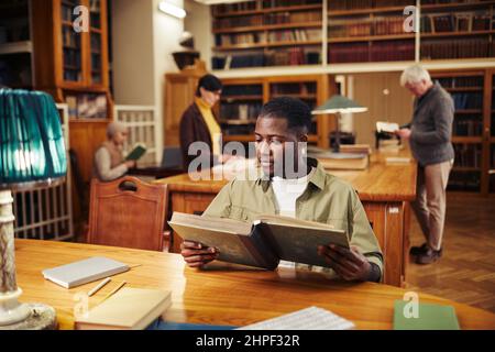 Portrait d'un jeune homme afro-américain qui lit un livre dans une bibliothèque universitaire classique tout en se préparant aux examens Banque D'Images