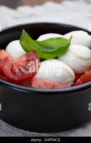 Cuisine italienne, savoureuse salade de caprese avec tomates cerises rouges, fromage mozzarella blanc et feuilles de basilic vert Banque D'Images