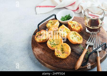 Délicieux muffins aux œufs avec oignons verts, bacon, fromage et tomates sur panneau de bois sur fond clair. Petit déjeuner sain à teneur élevée en protéines et faible en glucides. Banque D'Images