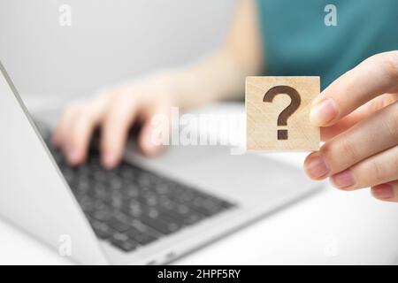 Présentation du concept de service à la clientèle et d'assistance. FAQ icône de point d'interrogation sur un cube en bois vue rapprochée, ordinateur portable sur une table de bureau blanche photo Banque D'Images