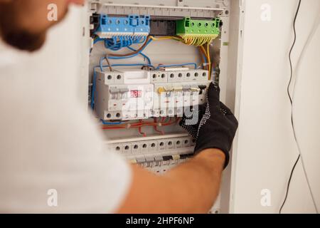 Main du technicien en électricité travaillant avec les fusibles au niveau de l'armoire de commande du disjoncteur sur le mur Banque D'Images