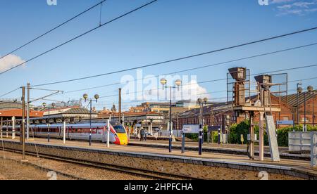 Deux trains se reposent sur une plate-forme de gare avec des canopies historiques au-dessus. Les voyants lumineux et un nom de lieu sont au premier plan. Banque D'Images