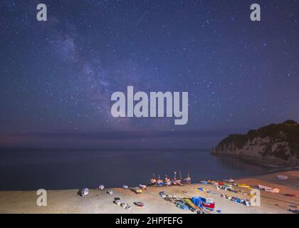 La voie lactée dans le ciel sud, vue depuis le front de mer à Beer, Devon, Angleterre, Royaume-Uni, avec des bateaux de pêche locaux tirés sur la plage en face, Banque D'Images