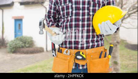 Section médiane d'un ouvrier de construction caucasien mâle portant une ceinture porte-outils tenant un casque et un marteau Banque D'Images