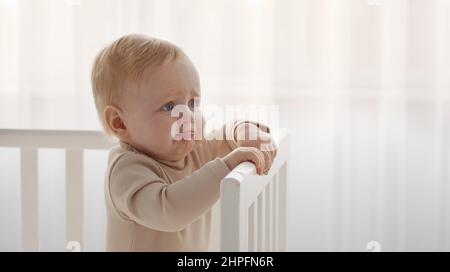 Portrait de bébé en pleurs. Petit bébé fatigué et affamé, commencez à pleurer debout dans le berceau, en regardant de côté à l'espace vide Banque D'Images