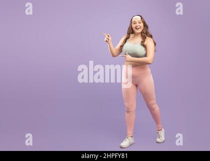 Joyeuse surprise plus grande taille de jeune femme européenne dans sportswear pointant du doigt sur l'espace libre Banque D'Images