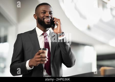 Bon directeur noir regardant avoir une conversation téléphonique, boire du café Banque D'Images