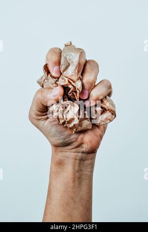 un homme presse une boule de papier brun froissé dans sa main sur un fond blanc cassé Banque D'Images