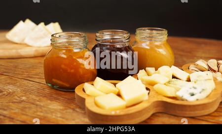 Des bocaux de confitures et de miel faits maison dans des bocaux en verre et une variété de fromages sur une table en bois. Assiette de fromages pour les hors-d'œuvre. Banque D'Images