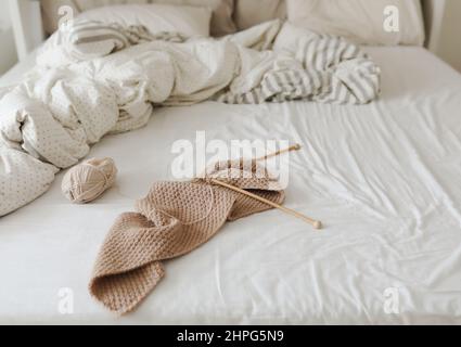 aiguilles à tricoter et fils de laine beige dans un lit confortable à la maison. Banque D'Images