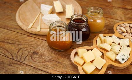 Des bocaux de confitures et de miel faits maison dans des bocaux en verre et une variété de fromages sur une table en bois. Assiette de fromages pour les hors-d'œuvre. Banque D'Images