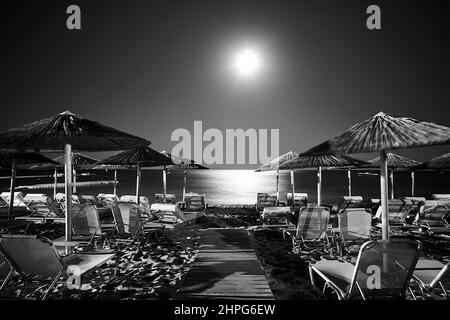 Transats et parasols vides sur la plage de sable sous la lune la nuit dans l'île de Zakynthos, Grèce , monochrome Banque D'Images