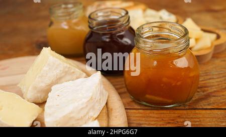 Des bocaux de confitures et de miel faits maison dans des bocaux en verre et une variété de fromages sur une table en bois. Assiette de fromages pour les hors-d'œuvre. Mise au point sélective Banque D'Images