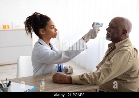 Travailleur médical noir effectuant un dépistage de la température chez le patient âgé Homme mesurant la fièvre avant la vaccination à l'aide d'un thermomètre infrarouge sans contact. COR Banque D'Images