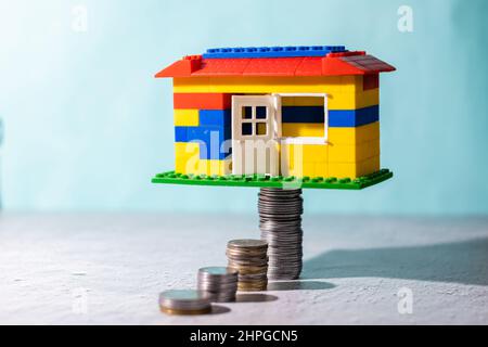 Une maison de jouets placée sur des piles de pièces de monnaie sur fond bleu: Concept d'épargne Banque D'Images