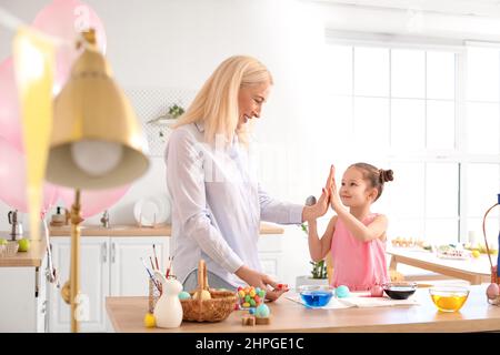 Bonne petite fille et sa grand-mère donnant cinq hauts l'un à l'autre tout en peignant des oeufs de Pâques à la maison Banque D'Images