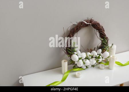 Belle couronne de Pâques et bougies sur la table près du mur lumineux Banque D'Images