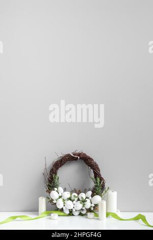 Belle couronne de Pâques et bougies sur la table près du mur lumineux Banque D'Images