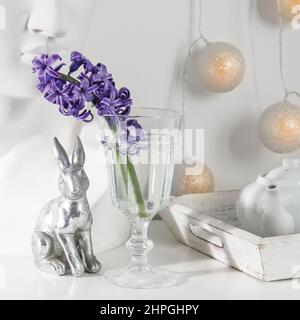 Figurines en céramique de lapins de Pâques de différentes tailles sur la table. Jacinthes bleu et blanc dans des tasses en verre sur fond blanc. Motif Pâques Banque D'Images