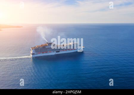 Bateau de croisière avec la fumée de la cheminée va à la mer ouverte au coucher du soleil Banque D'Images