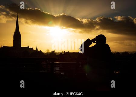 SALISBURY, ROYAUME-UNI. Un homme regarde le soleil se coucher sur la cathédrale de Salisbury dans des conditions beaucoup plus calmes après des jours de vents forts et de fortes pluies à Wiltshire, Royaume-Uni. Daté du 21/02/2022. Crédit : Matthew Lofthouse/Alamy Live News Banque D'Images