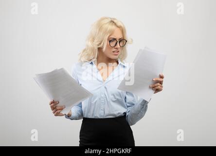 Concept de paperasserie. Femme d'affaires concentrée dans des lunettes lisant des documents sur fond gris clair de studio Banque D'Images