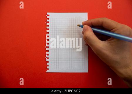 Tenez le stylo à la main et écrivez sur du papier vierge. Isolé sur fond rouge. Banque D'Images