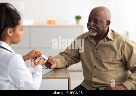 Concept de bouton d'urgence. Portrait d'un professionnel de la santé noir tenant le bouton d'alarme personnel et le donnant à un patient âgé, assis à une table au bureau. Banque D'Images