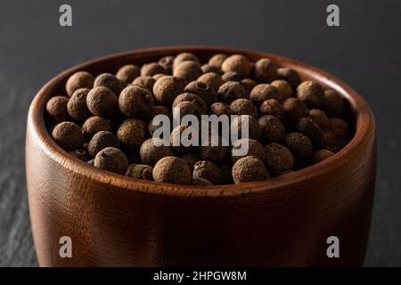 Bol en bois plein de grains de poivre de jamaïque d'épice. Gros plan sur les baies brunes séchées de l'arbre Pimenta dioica. Concept de piment entier pour les épices biologiques. Banque D'Images