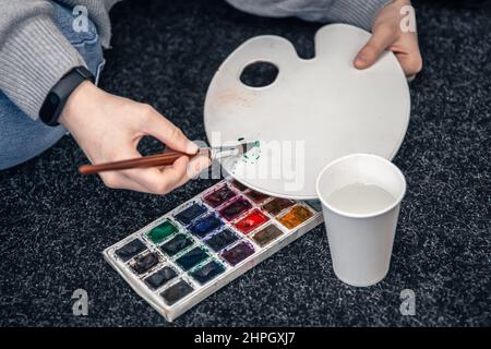 Gros plan d'une palette de peintures et d'un verre d'eau. Banque D'Images