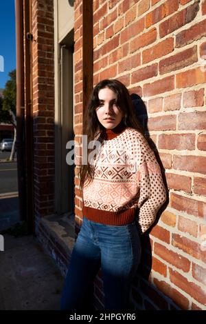 Jeune femme en vêtements rétro debout devant un mur de briques Banque D'Images