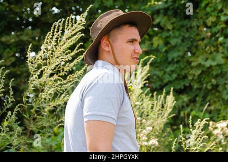 Homme en chapeau.Portrait d'un fermier souriant avec de l'herbe verte et de la nature des arbres en arrière-plan.Jeune homme portant un chapeau de cow-boy sur le terrain.Gros plan.Joyeux jeune p Banque D'Images