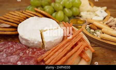 Différents hors-d'œuvre savoureux sur fond de bois. Assiette de fromage et de viande. Saucisses, fromage, noix, raisins, crackers. Concentrez-vous sur le fromage Camembert Banque D'Images