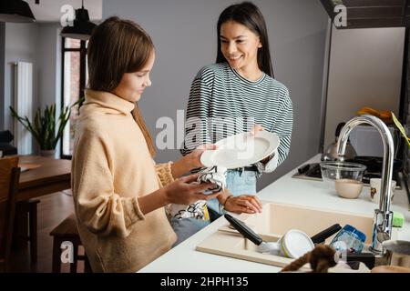 Bonne belle mère et fille souriante et lave les plats dans la cuisine confortable Banque D'Images