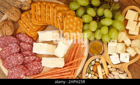 Différents hors-d'œuvre savoureux sur fond de bois, vue de dessus. En-cas pour le vin. Assiette de fromage et de viande. Saucisses, fromage, noix, raisins, crackers Banque D'Images