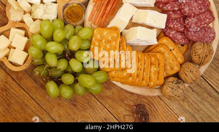 Différents hors-d'œuvre savoureux sur fond de bois, vue de dessus. En-cas pour le vin. Assiette de fromage et de viande. Saucisses, fromage, noix, raisins, crackers Banque D'Images