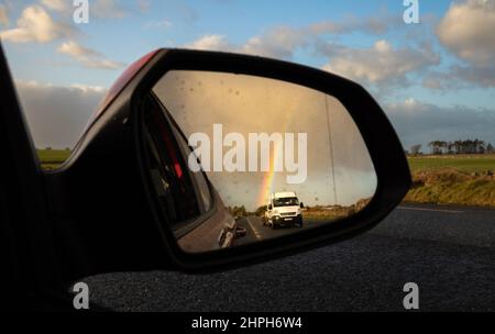 Une fourgonnette blanche et un arc-en-ciel sont vus dans le rétroviseur latéral d'une voiture roulant en Irlande. Banque D'Images