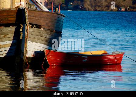 Petit bateau en bois rouge ancré à côté d'un vieux bateau de pêche marron dans un port. Banque D'Images