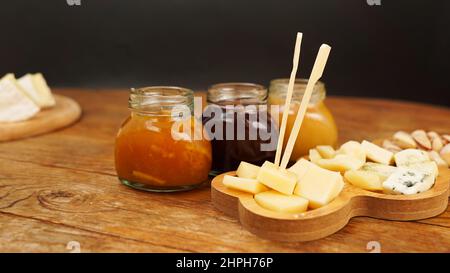 Pots de confiture et de miel faits maison dans des pots en verre et une variété de fromages sur une table en bois. Assiette de fromages pour les hors-d'œuvre. Banque D'Images