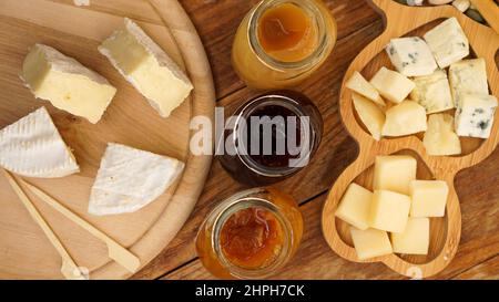 Des bocaux de confitures et de miel faits maison et une variété de fromages sur une table en bois. Assiette de fromages pour hors-d'œuvre avec brochettes en bois pour la nourriture. Vue de dessus Banque D'Images
