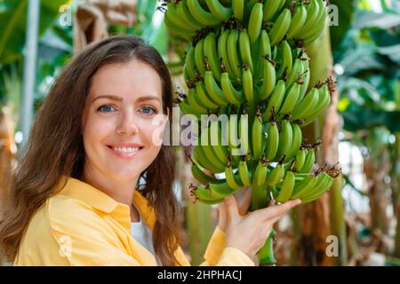 Bonne femme souriante paysanne agronome contrôle la culture de bouquet de bananes fruits récolte de jeunes palmiers contre la plantation, jardin tropical Banque D'Images