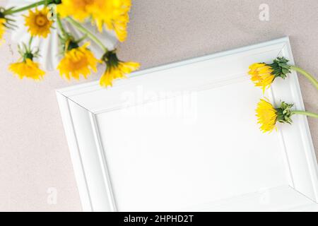 Maquette de cadre blanc avec fleurs de pissenlit jaune sauvage dans un vase et une boîte en coton. Maquette avec cadre vide pour un motif de présentation. Modèle avec blanc s vierge Banque D'Images